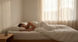Person sleeping peacefully on their side in a minimalist bedroom with soft morning light through linen curtains