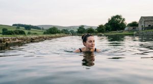 Young woman swimming in a calm outdoor lido in the English countryside, head above water, soft overcast light